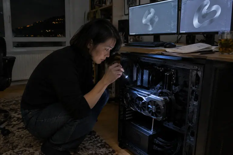 Une femme vérifie à la lampe que le connecteur 16 broches est bien enfoncé dans une très grande carte graphique, dans un boîtier ouvert