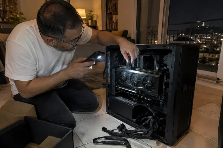 Tard le soir, un homme branche le câble 16 broches d’une grande carte graphique et vérifie à la lampe de son téléphone qu’il est bien enfoncé