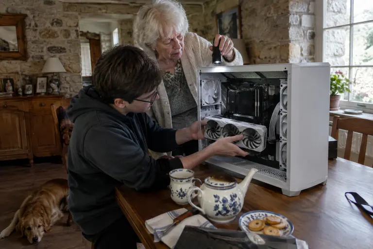 Une grand-mère éclaire à la lampe de poche le PC blanc dans lequel son petit-fils installe une carte graphique blanche à trois ventilateurs