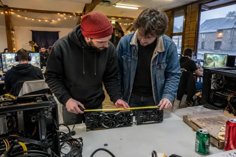 Deux amis comparent une longue carte graphique à trois ventilateurs et une carte plus courte à deux ventilateurs lors d’une LAN party