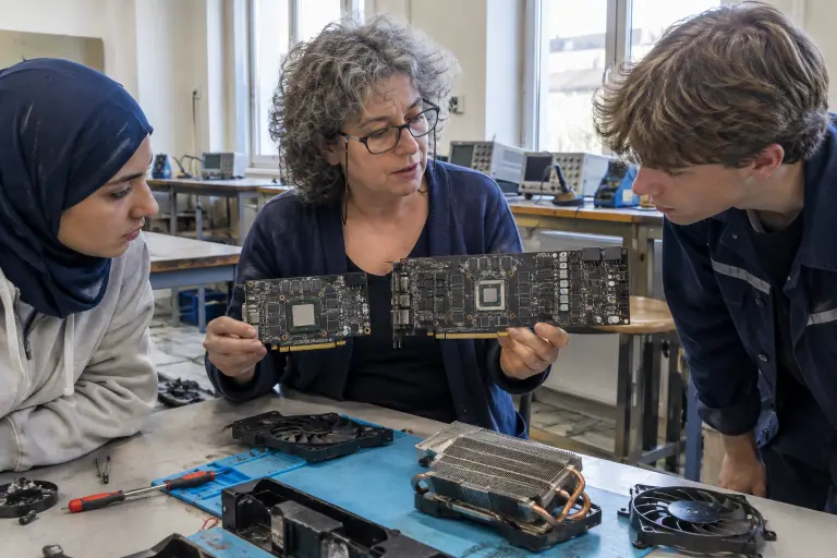 Dans un lycée professionnel de Limoges, une enseignante montre à deux élèves deux circuits de cartes graphiques nus, l’un à 4 puces mémoire, l’autre à 12