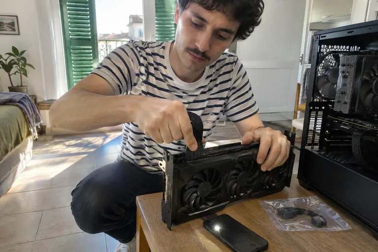 Un jeune homme enfonce du pouce le câble 16 broches d’une carte graphique à trois ventilateurs, l’adaptateur resté dans son sachet