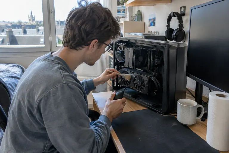 Dans une chambre étudiante à Caen, un jeune homme dépoussière au pinceau les ventilateurs de sa carte graphique, boîtier ouvert sur son bureau