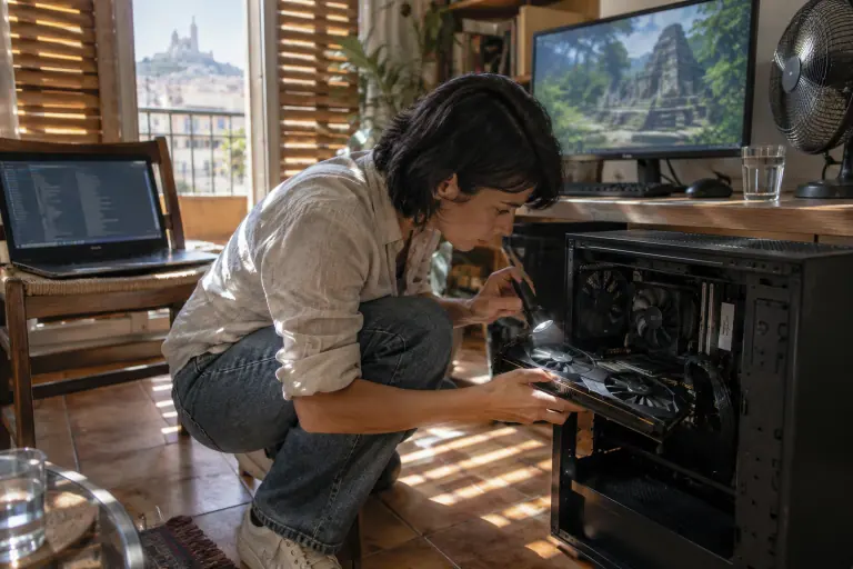 À Marseille, une femme vérifie à la lampe torche la carte graphique de son PC ouvert, devant un écran montrant des ruines dans la jungle