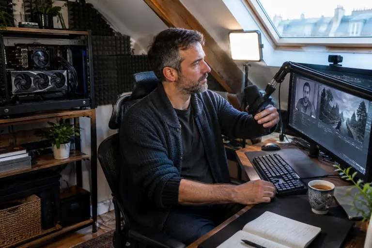 Dans un studio sous les toits à Paris, un streamer règle son micro sur bras articulé devant deux écrans, avec un PC à grande carte graphique sur une étagère