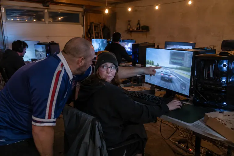 Pendant une LAN entre amis dans un garage, un homme montre à son amie le compteur de performances affiché dans un coin de son écran de jeu