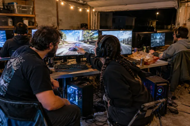 Lors d’une LAN party dans un garage à Nantes, un joueur barbu montre son écran à sa voisine en casque pour comparer la fluidité d’un jeu de course