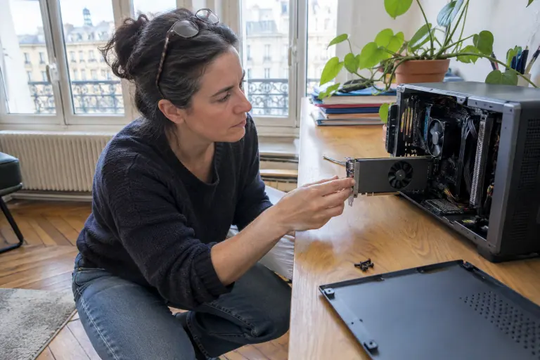 Dans un bureau à Bordeaux, une femme glisse une petite carte graphique low profile dans un PC de bureau compact ouvert et couché sur la table