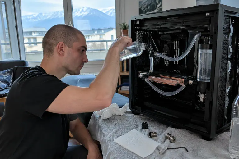 Un jeune homme remplit le circuit de watercooling de son PC, relié à une carte graphique très fine équipée d’un bloc en cuivre, à Grenoble