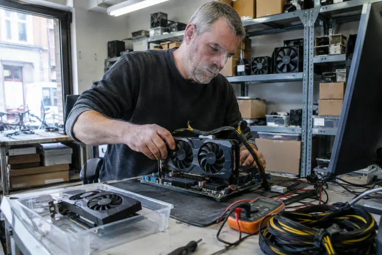 Un technicien teste une carte graphique d’occasion à deux ventilateurs sur un banc d’essai ouvert, dans l’atelier d’une petite boutique informatique