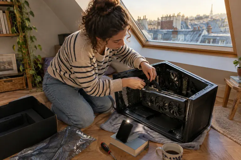Sous les toits de Paris, une jeune femme branche le câble d’alimentation 16 broches d’une grande carte graphique installée dans un PC ouvert