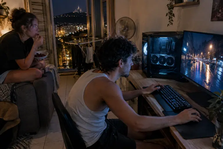 À Marseille, un jeune homme joue à un jeu aux reflets de pluie très réalistes pendant que sa sœur regarde l’écran depuis le canapé