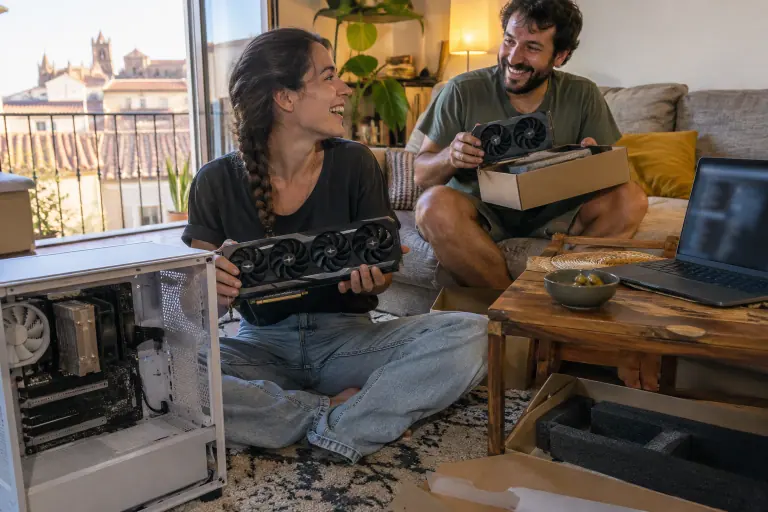 Dans un appartement de Montpellier, un couple hésite en riant entre une grande carte graphique à trois ventilateurs et un modèle plus compact