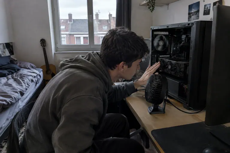 Dans une chambre d’étudiant à Lille, un jeune homme approche la main d’une carte graphique à trois ventilateurs pour en sentir la chaleur