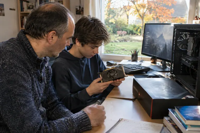 Un père et son fils adolescent examinent une ancienne carte graphique compacte, une nouvelle carte encore dans sa boîte posée sur le bureau