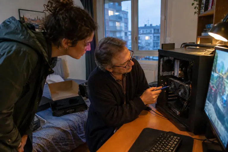 Une acheteuse examine une carte graphique d’occasion à deux ventilateurs qui tourne dans le PC ouvert du vendeur, chez lui, avant de l’acheter