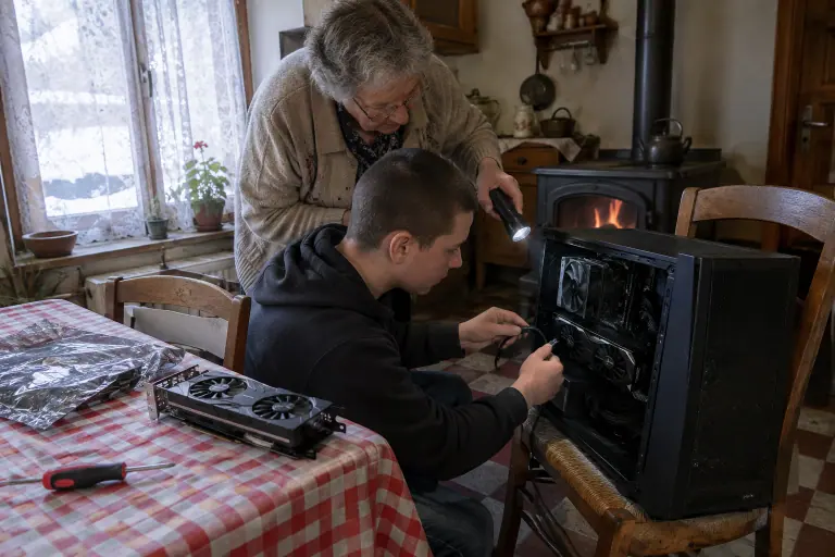 Un adolescent branche le câble 8 broches d’une carte graphique compacte dans une vieille tour, éclairé par sa grand-mère qui tient une lampe de poche