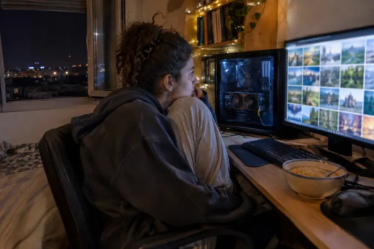 Une étudiante assise en tailleur regarde des images générées s’afficher sur son écran, à côté d’un PC vitré équipé d’une carte à deux ventilateurs