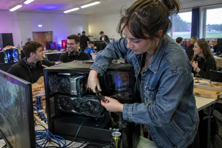 Lors d’une LAN party dans une salle des fêtes, une joueuse branche les câbles 8 broches d’une longue carte graphique à trois ventilateurs