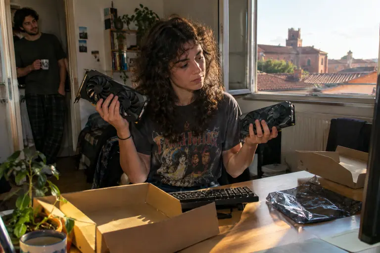 Dans une colocation à Toulouse, une étudiante tient deux petites cartes graphiques à deux ventilateurs, une dans chaque main, devant son bureau