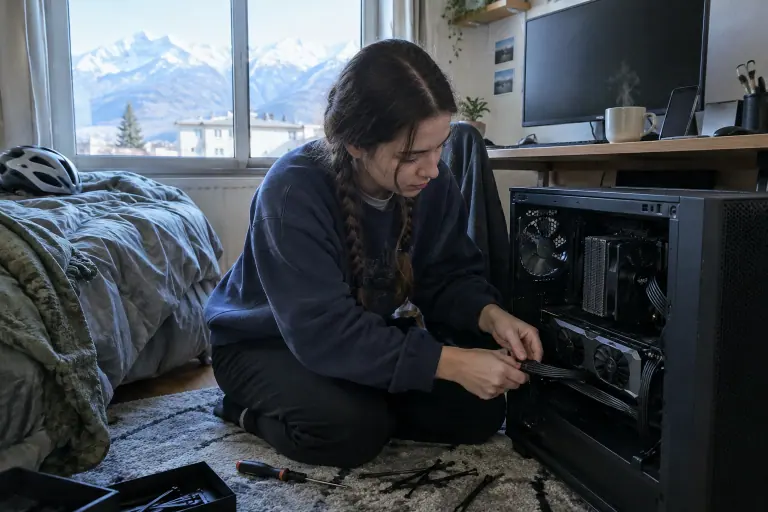 Dans une chambre d’étudiante à Grenoble, une jeune femme branche l’adaptateur 16 broches d’une carte graphique à deux ventilateurs dans un boîtier ouvert