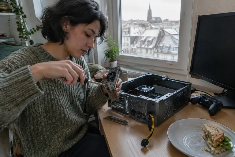 Une jeune femme change l’équerre d’une carte graphique demi-hauteur avant de l’installer dans un PC de bureau compact ouvert sur sa table de travail