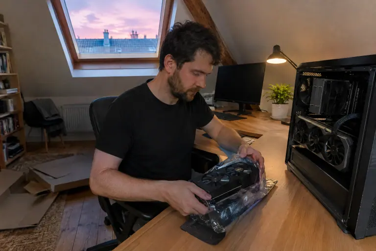 Sous les toits de Paris, un homme range son ancienne carte graphique dans un sachet antistatique, la nouvelle déjà installée dans son PC ouvert