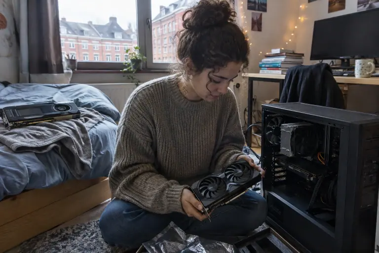 Dans une chambre d’étudiante à Lille, une jeune femme assise par terre tient une carte graphique compacte à côté de son PC ouvert
